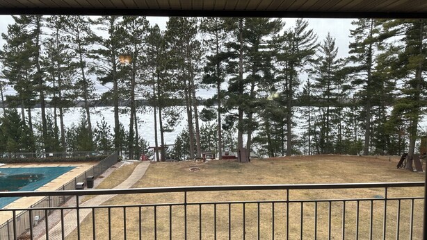 A view from a balcony overlooking a swimming pool, a grassy area, and a forested landscape.