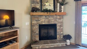 A stone fireplace with a mounted mirror, a ceiling fan, and a TV on a stand.