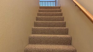 A carpeted staircase with a wooden handrail, leading to a balcony with a railing.