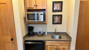 A compact kitchenette with a microwave, coffee maker, sink, and dishwasher.