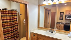 A bathroom with a striped shower curtain, wooden cabinets, a sink, and a large mirror.
