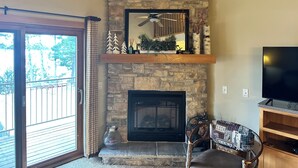 A living room with a stone fireplace, a mounted television, and a balcony with a view of trees. - Spirit of the Northwoods (eagle river)