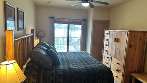 A bedroom with a bed, a wooden dresser, a ceiling fan, a window with curtains, and a lamp. - Spirit of the Northwoods (eagle river)