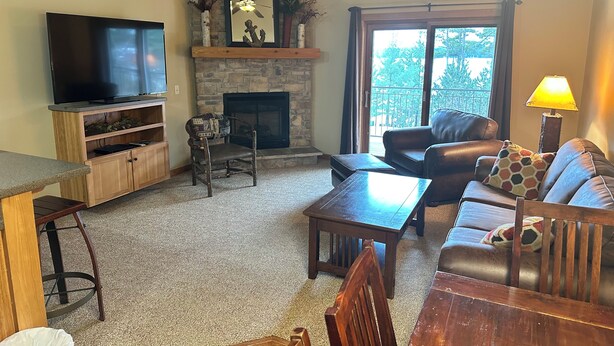 A living room with a stone fireplace, leather sofa, wooden coffee table, and a TV on a wooden stand. - CONDO 305/LOFT by Eagle Waters Resort (eagle river)