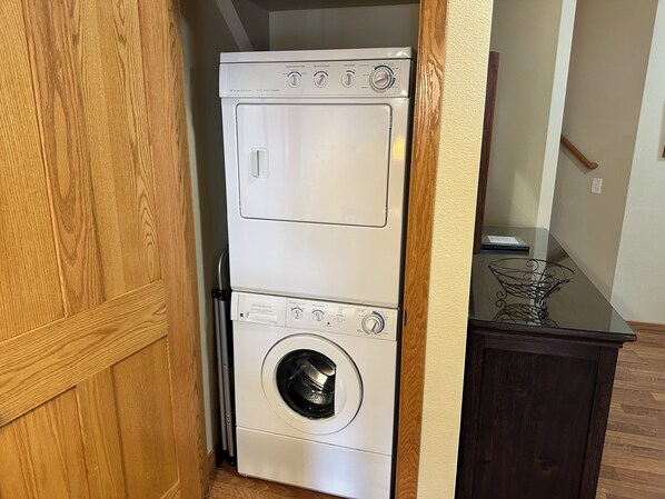 A compact washer and dryer unit in a small laundry room with wooden cabinetry and a dark countertop.