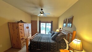 Une chambre à coucher avec un lit, une armoire en bois, un ventilateur de plafond et une table avec une lampe.