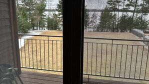 A view through a window with a metal railing, a wooden deck, and a snowy landscape with trees in the background.