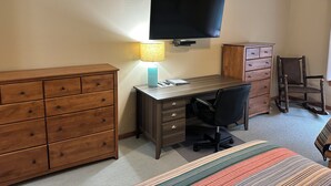 A hotel room with a wooden desk, a chair, a television mounted on the wall, a lamp, a dresser, and a bed with a striped blanket. - Studio 316 By Eagle Waters Resort (eagle river)
