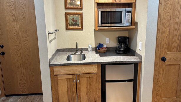 A compact kitchen with wooden cabinets, a stainless steel sink, a microwave, and a coffee maker. - Studio 316 By Eagle Waters Resort (eagle river)