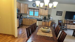 Una cocina amplia con armarios de madera, una mesa de comedor con sillas, una araña y un televisor en la sala.