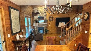 A wooden interior with a dining table, chairs, a fireplace, a clock, and a chandelier. - Cabin 16D by Eagle Waters Resort (eagle river)