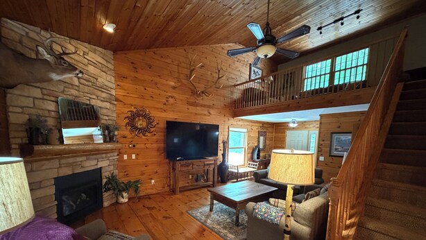 A log cabin interior with a stone fireplace, wooden floors, a television, and a staircase leading to an upper level. - Cabin 16D by Eagle Waters Resort (eagle river)