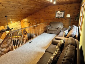 Cozy cabin interior with a plush sofa, comfortable armchair, and wooden staircase.