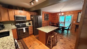 A kitchen with granite countertops, stainless steel appliances, wooden cabinets, and a dining area with a wooden table and chairs. - Cabin 16D by Eagle Waters Resort (eagle river)