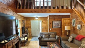 A cozy cabin interior with a large TV, wooden furniture, a staircase, and a door leading to another room. - Cabin 16D by Eagle Waters Resort (eagle river)