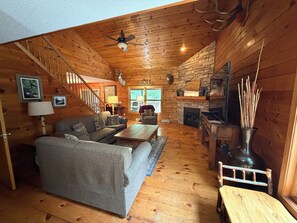 Ein Holzblockhaus-Interieur mit einer Couch, einem Couchtisch, einem Kamin und einer Treppe.
