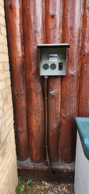 A utility box mounted on a wooden wall with a metal conduit extending from it.