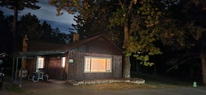 A rustic cabin with a covered porch, a stone chimney, and a number '3939' sign.