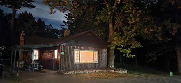 A rustic cabin with a covered porch, a stone chimney, and a number '3939' sign.