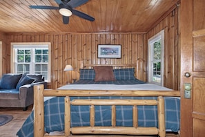 A wooden-paneled room with a bed, a sofa, and a ceiling fan.