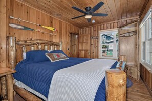 A wooden cabin bedroom with a bed, a ceiling fan, and a window.