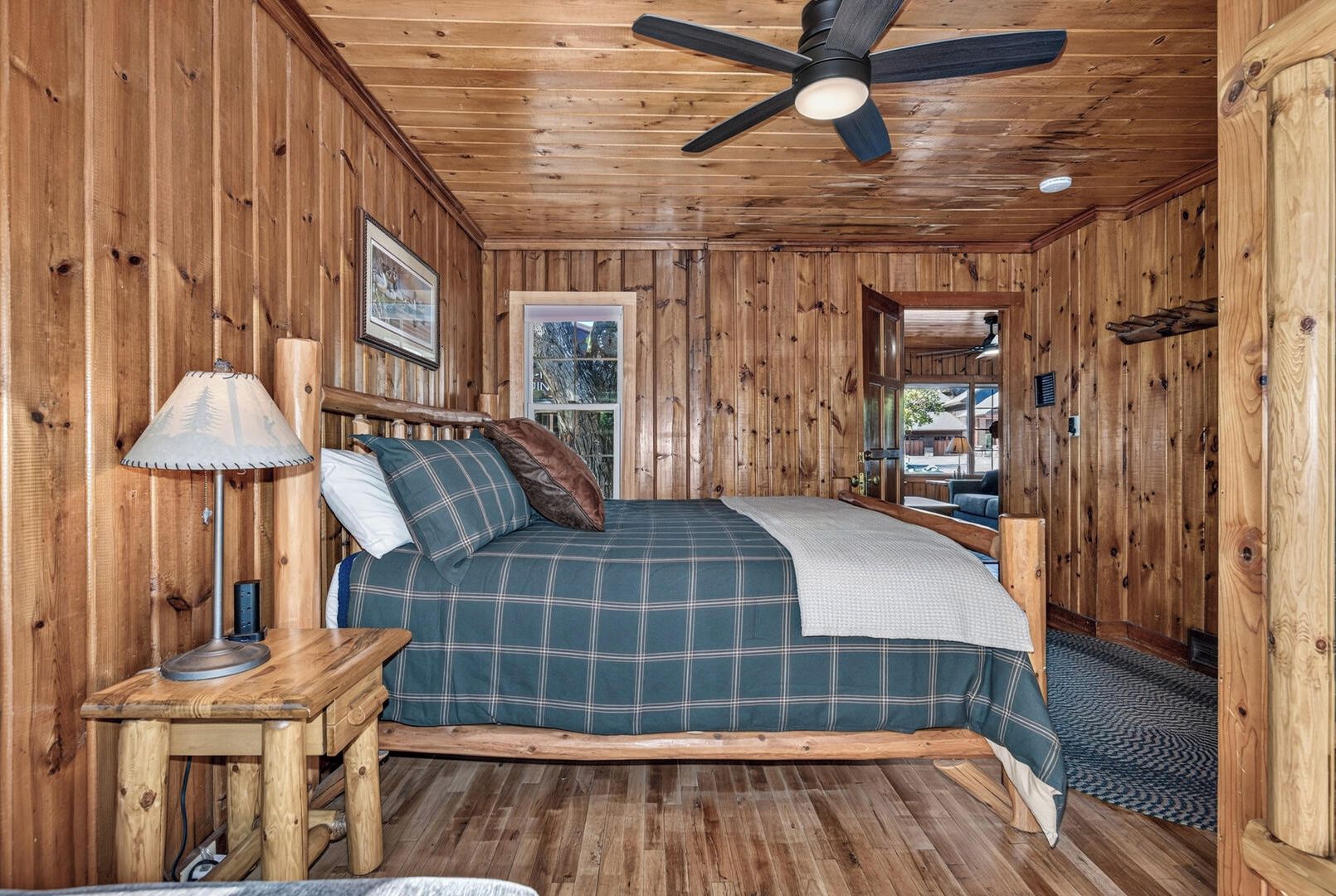 Cozy up in your rustic wood-wrapped bedroom, where natural pine walls and a warm ceiling fan create a peaceful retreat. Soft lighting and a glimpse of greenery outside invite you to unwind after a day of adventure.