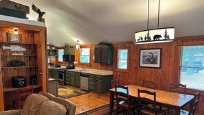 A cozy cabin-style kitchen with wooden walls, a dining area with a table and chairs, and a living room with a leather couch. - Cabin 3 by Eagle Waters Resort (eagle river)