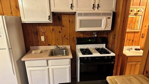 Una cocina compacta con armarios blancos, un microondas, una estufa y un refrigerador.