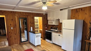 Una cocina compacta con paredes de madera, armarios blancos, estufa y refrigerador.