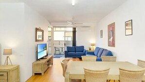 A modern living room with a television, blue sofa, dining table, and wicker chairs.