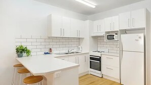 A modern kitchen with white cabinets, a central island with stools, a microwave, and an oven.