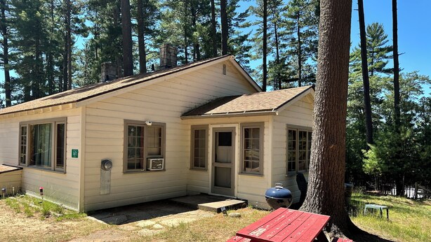 A small cabin with a single door and windows, a picnic table, and a grill nearby. - Cabin 14A by Eagle Waters Resort (eagle river)