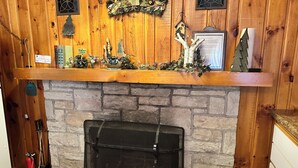 A stone fireplace with a metal screen, wooden mantel with holiday decorations, and a 'Relax Cabin' sign. - Cabin 14A by Eagle Waters Resort (eagle river)