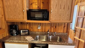 A compact kitchen with wooden cabinets, a microwave, a toaster, a sink, and a trash bin. - Cabin 14A by Eagle Waters Resort (eagle river)