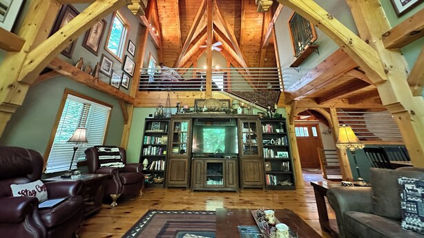 A spacious living area with wooden beams, a fireplace, and a staircase leading to an upper level.