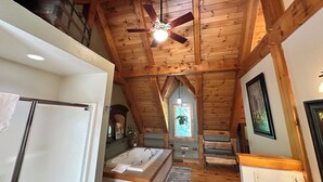 A spacious attic bedroom with a large window, a ceiling fan, and a built-in bathtub.