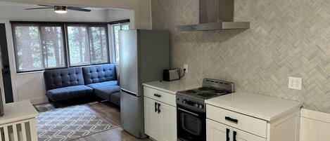 A compact kitchen with a built-in stove, oven, and microwave, a seating area with a sofa, and a window providing natural light.