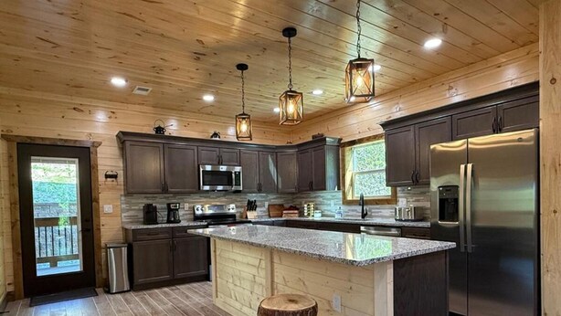 A modern kitchen with dark wood cabinets, stainless steel appliances, and a central island with stools.