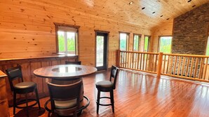 A spacious room with a wooden floor, a round table with chairs, and a stone accent wall.