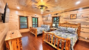 A log cabin room with two wooden beds, a wooden table, and a ceiling fan.