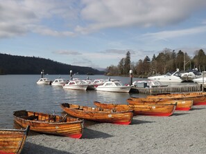 A marina with several wooden boats docked on the shore and a few larger boats in the water. - Two West End (Windermere)