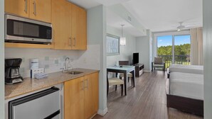 A modern kitchen with wooden cabinets, a built-in microwave, and a coffee maker. There is a dining area with a table and chairs, and a balcony with a view of the trees. - Studio Condo in Luxe Sandestin Resort w/ Balcony, Pool, + Walk to Baytowne Wharf (Miramar Beach)