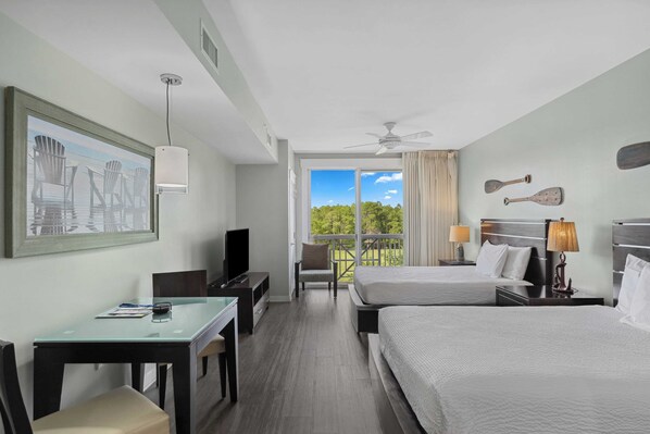 A hotel room with two beds, a desk, a chair, a TV, and a balcony with a view of trees. - Studio Condo in Luxe Sandestin Resort w/ Balcony, Pool, + Walk to Baytowne Wharf (Miramar Beach)