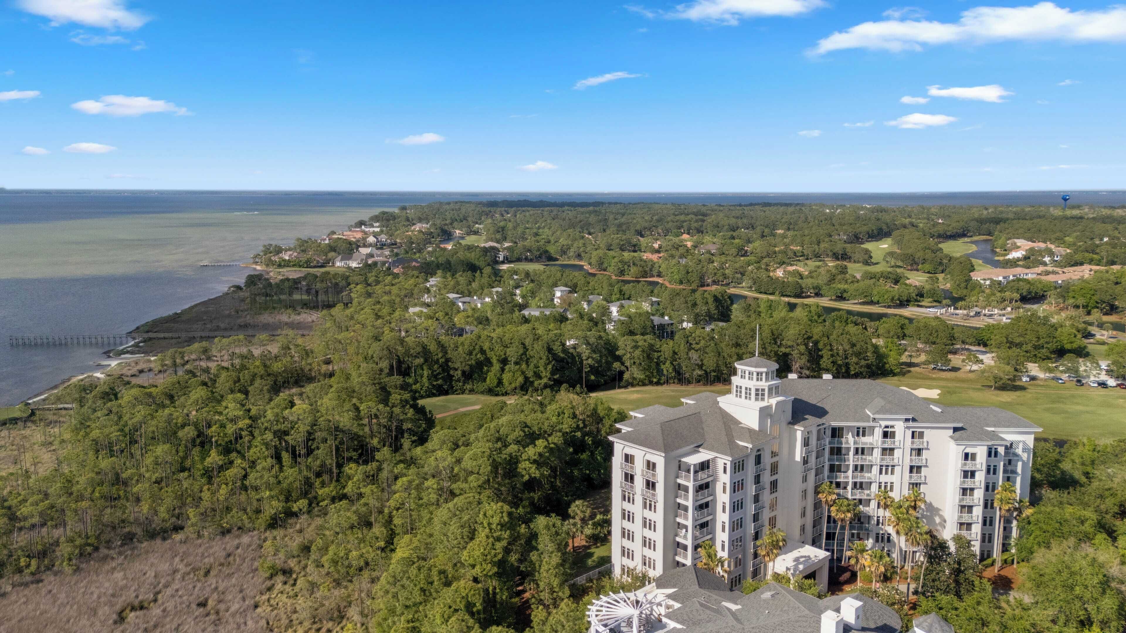 A large resort with multiple buildings, including a prominent tower, surrounded by lush greenery and a body of water.