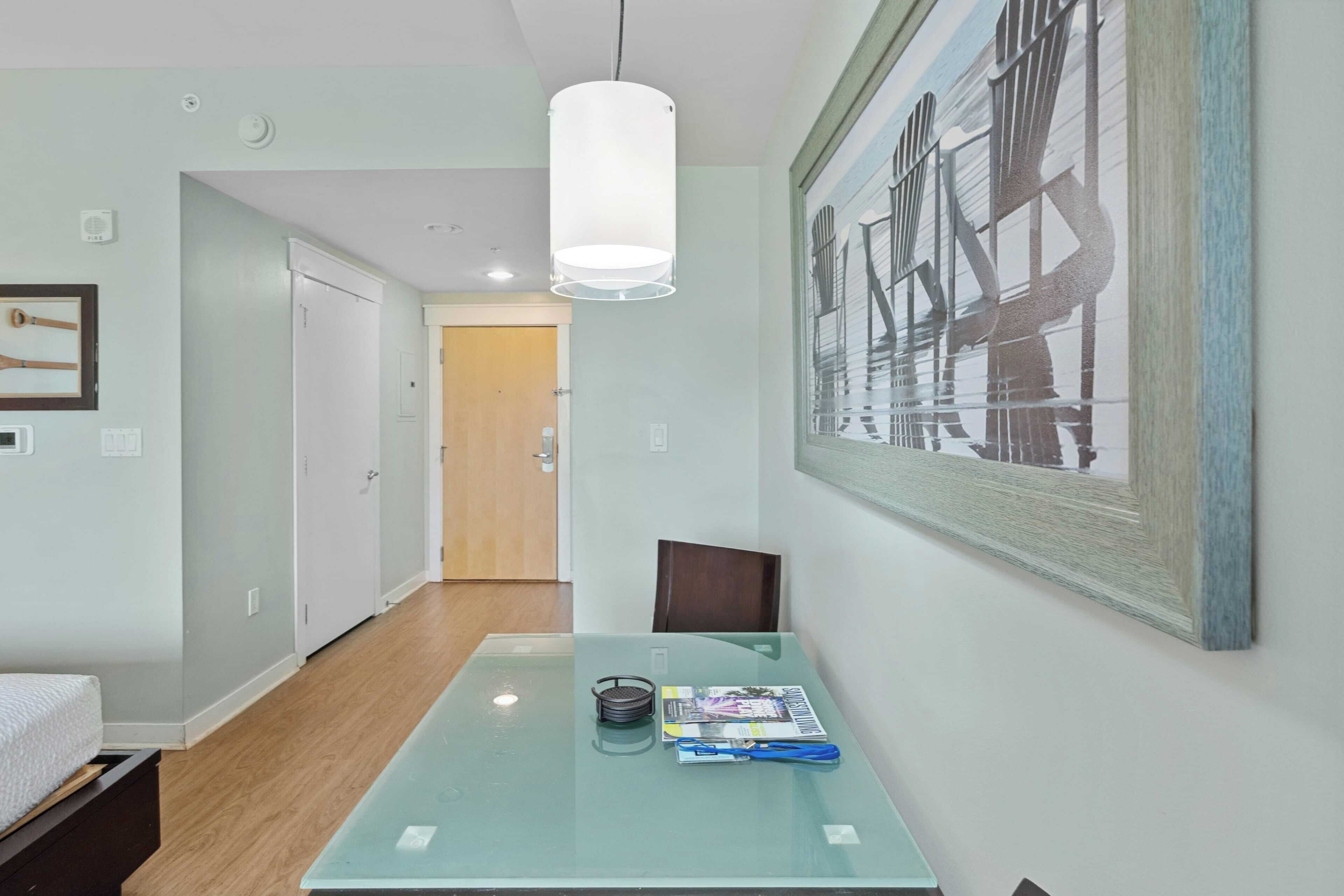 A modern hotel room with a glass table, a framed artwork on the wall, and a wooden floor.