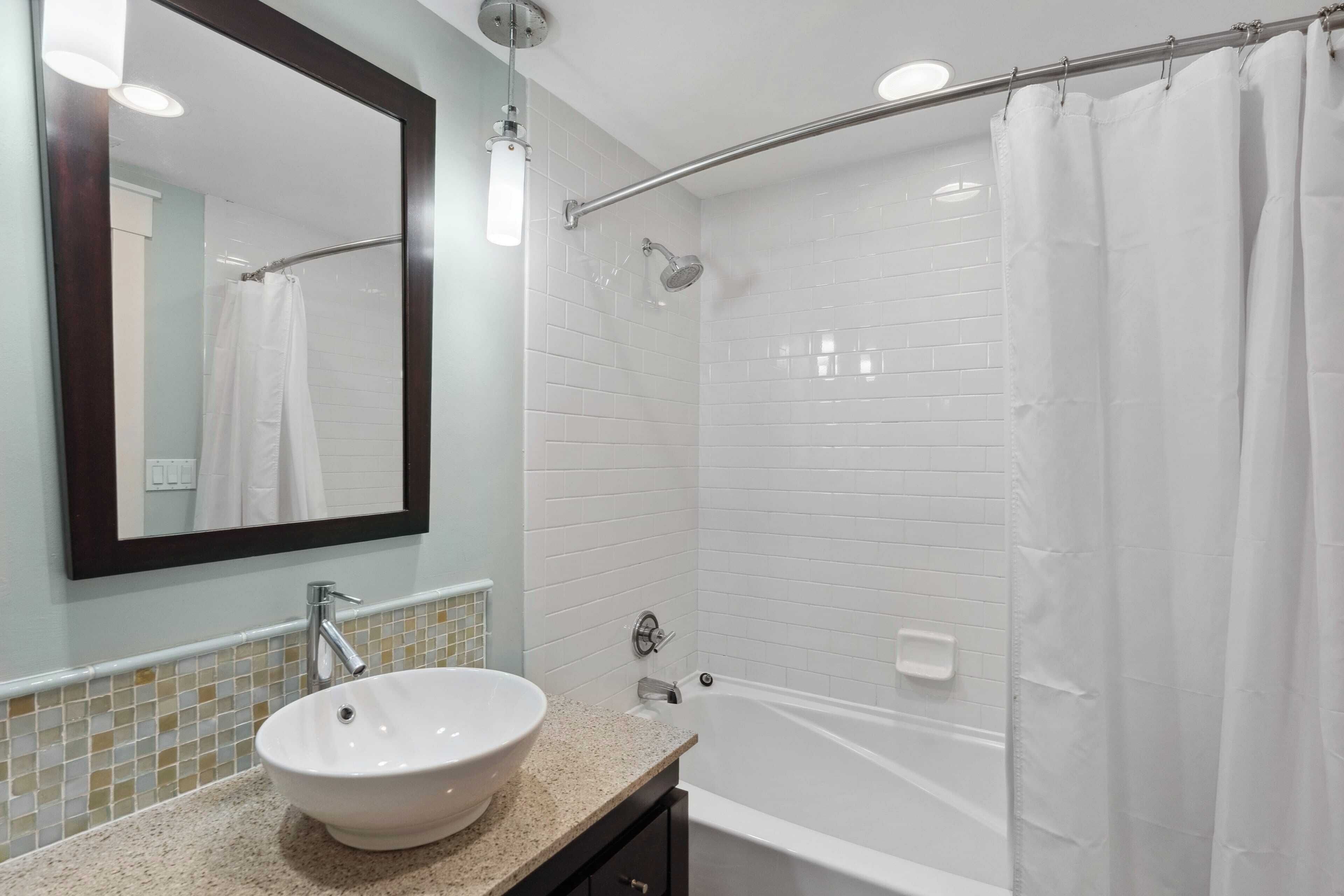 Een badkamer met een witte wastafel, een spiegel, een douche met glazen deur en een bad.