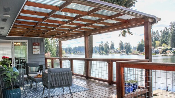 Une terrasse en bois agrémentée d’une pergola, d’un espace salon et offrant une vue sur un lac.