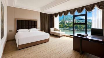 A hotel room with a bed, a desk, a chair, and a large window with a view.