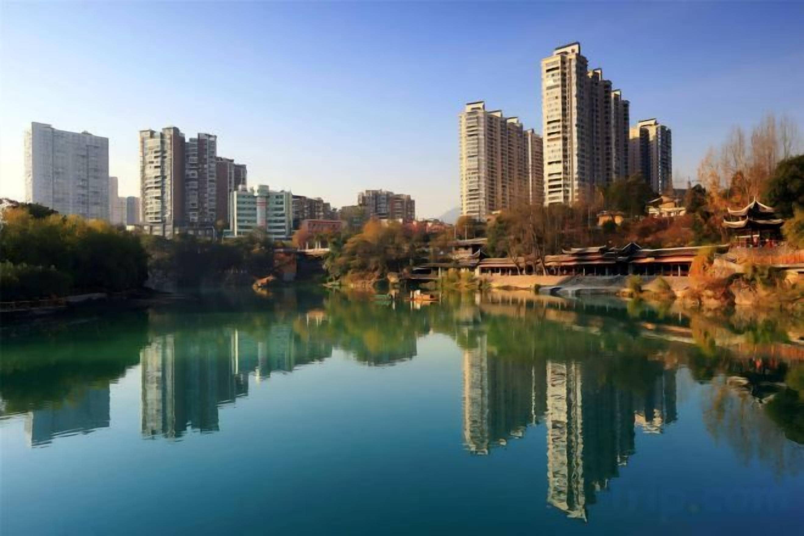 A calm lake reflecting buildings, including high-rise apartments and traditional architecture.