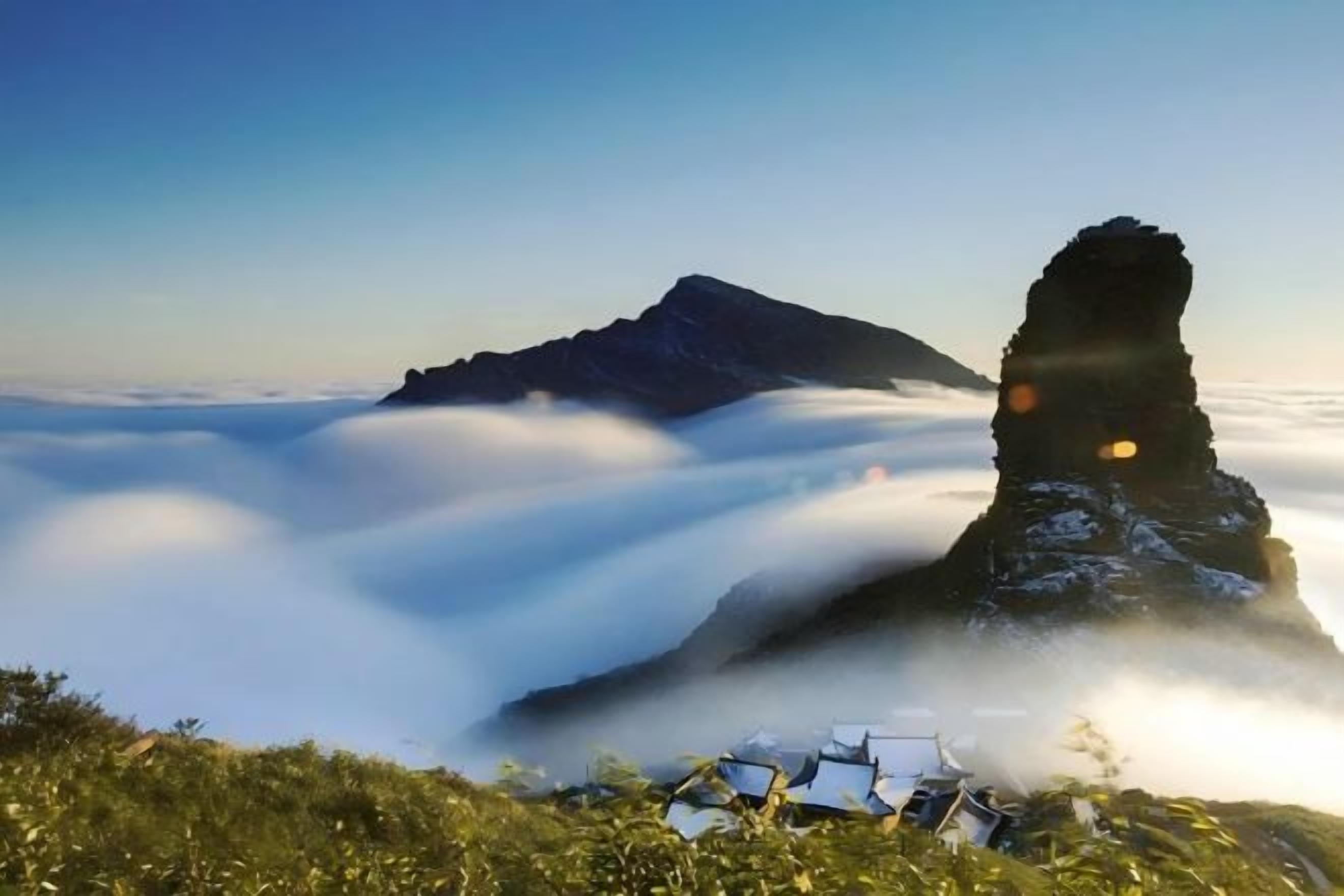 A mountain peak with a unique rock formation, surrounded by clouds, and a small structure at the base.